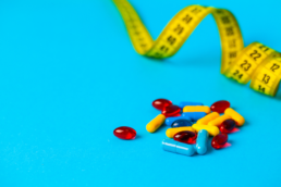 A pile of pills lies on a blue tabletop next to a measuring tape, symbolizing GLP-1 agonist side effects.