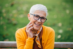 A woman with short, gray hair laughs with her hand on her face, representing women’s peri- and postmenopausal sexual health.