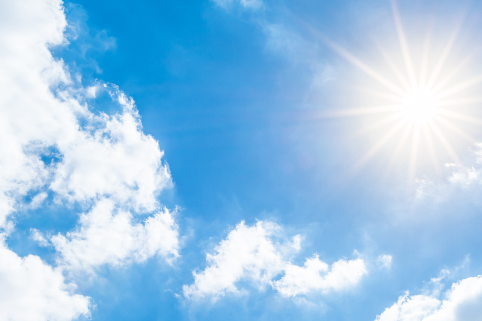 A bright blue sky with fluffy white clouds and bright sunshine symbolizes the connection between light, health, and wellness.