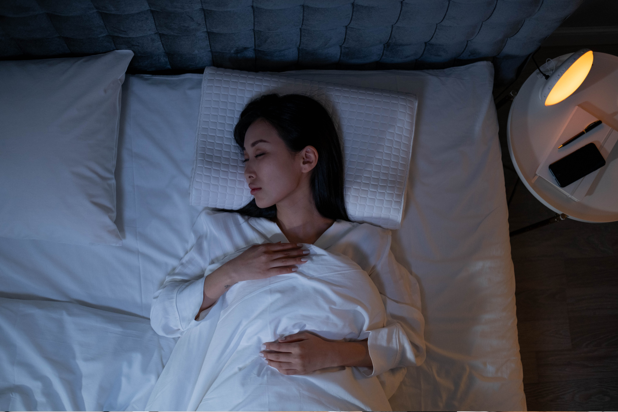Woman sleeping peacefully in dark bedroom with nightstand lamp on.