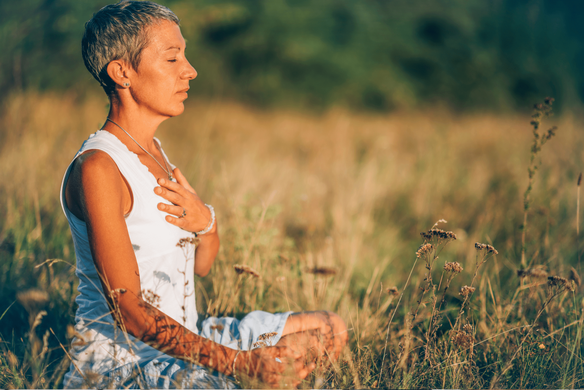 Person meditating outdoors in nature, breathing mindfully with hand on chest.
