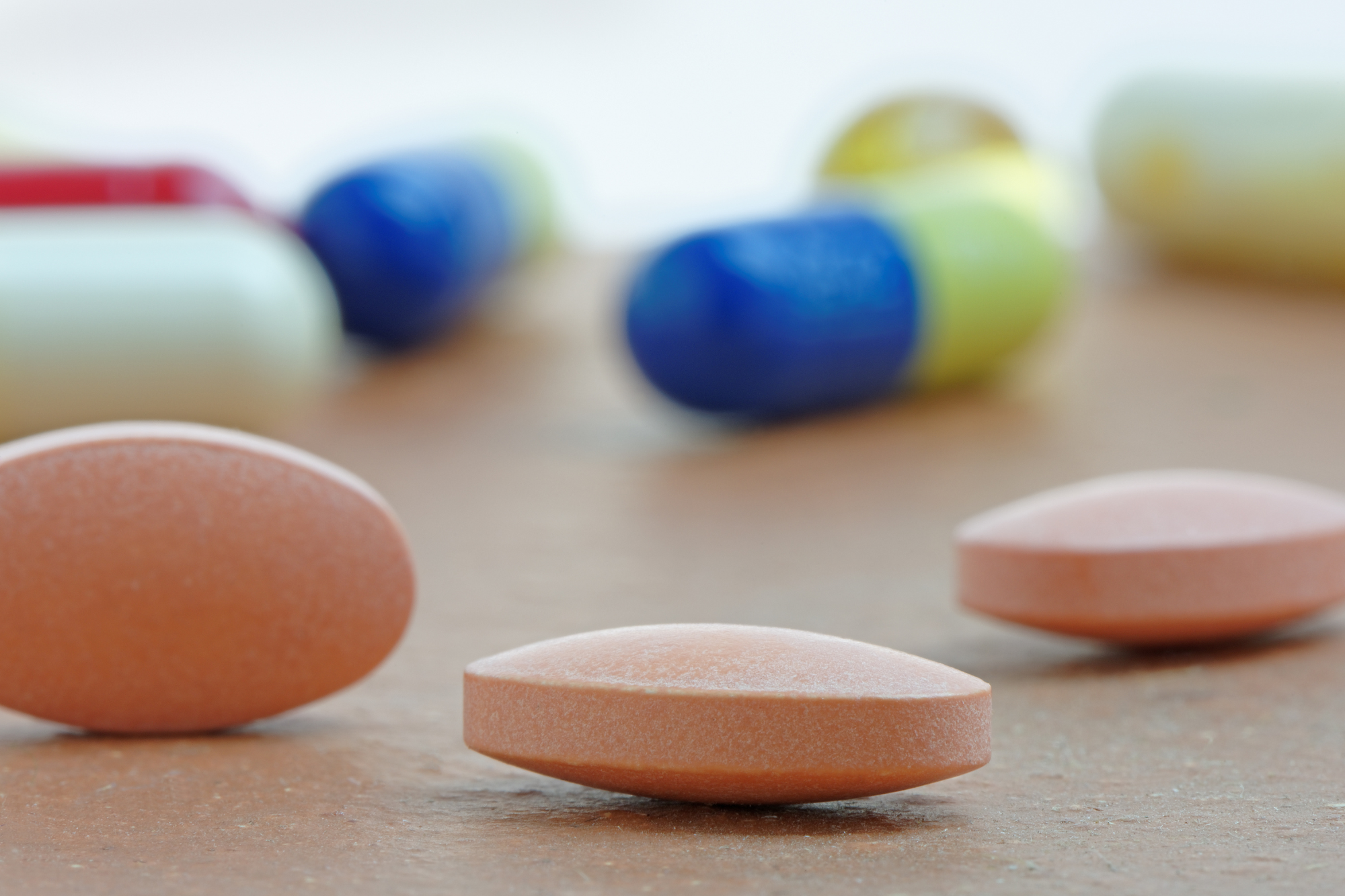 Three statin pills for cholesterol sit close on a wooden table, with out-of-focus pills lying in the background.