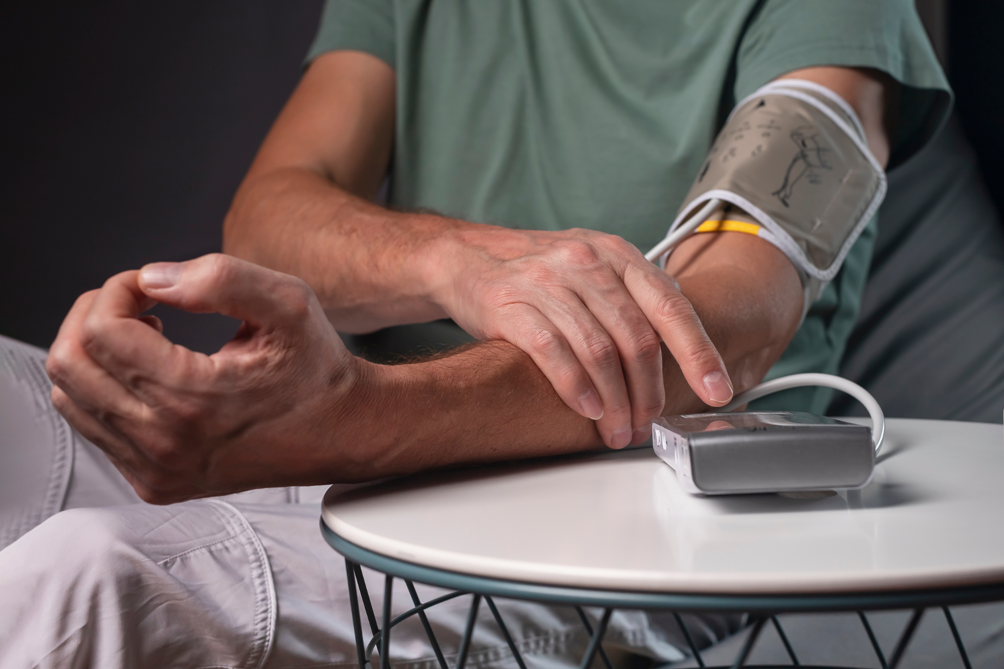 A man sits in a chair while measuring his blood pressure at home with a reliable blood pressure cuff.