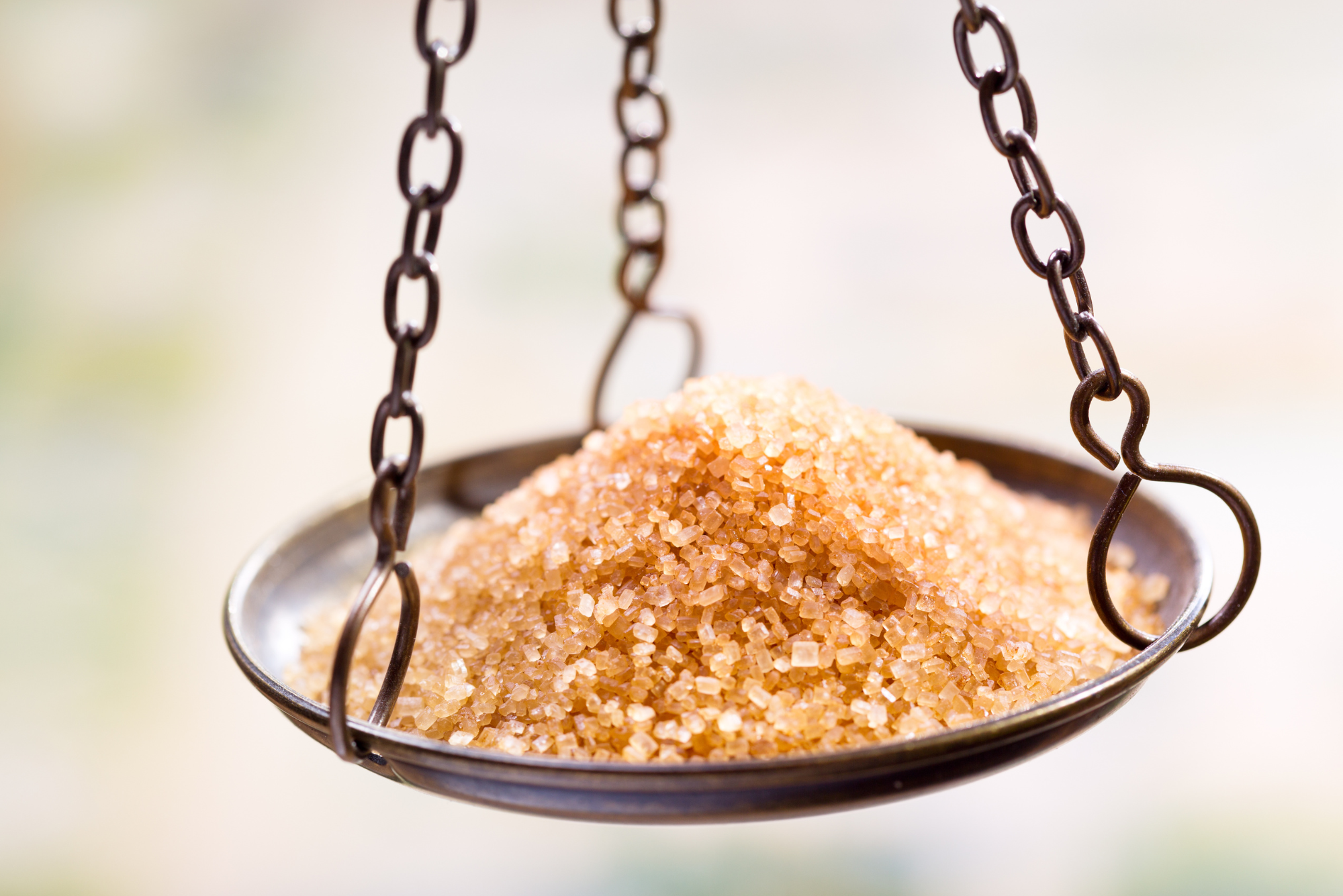 A metal balance scale cup full of light brown sugar crystals.