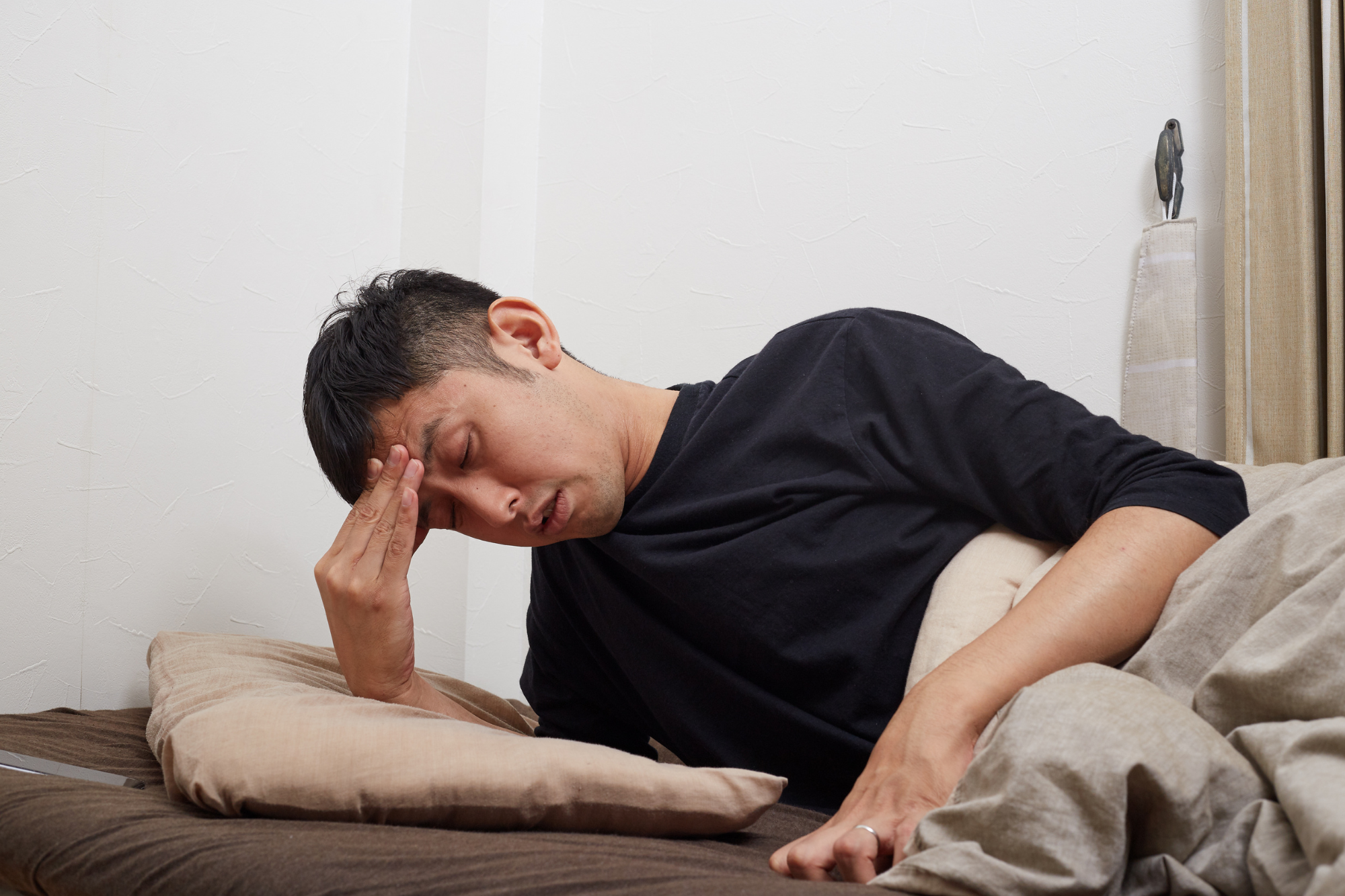 A man winces in pain while resting his head on finger tips, experiencing a hangover headache.