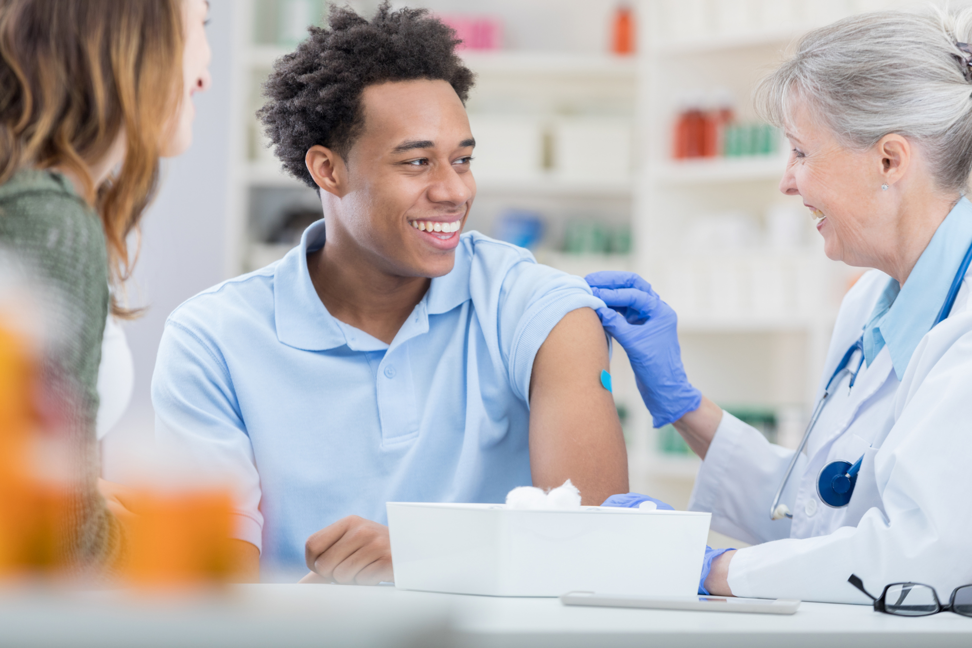 Young man smiling while receiving vaccination from senior female doctor.