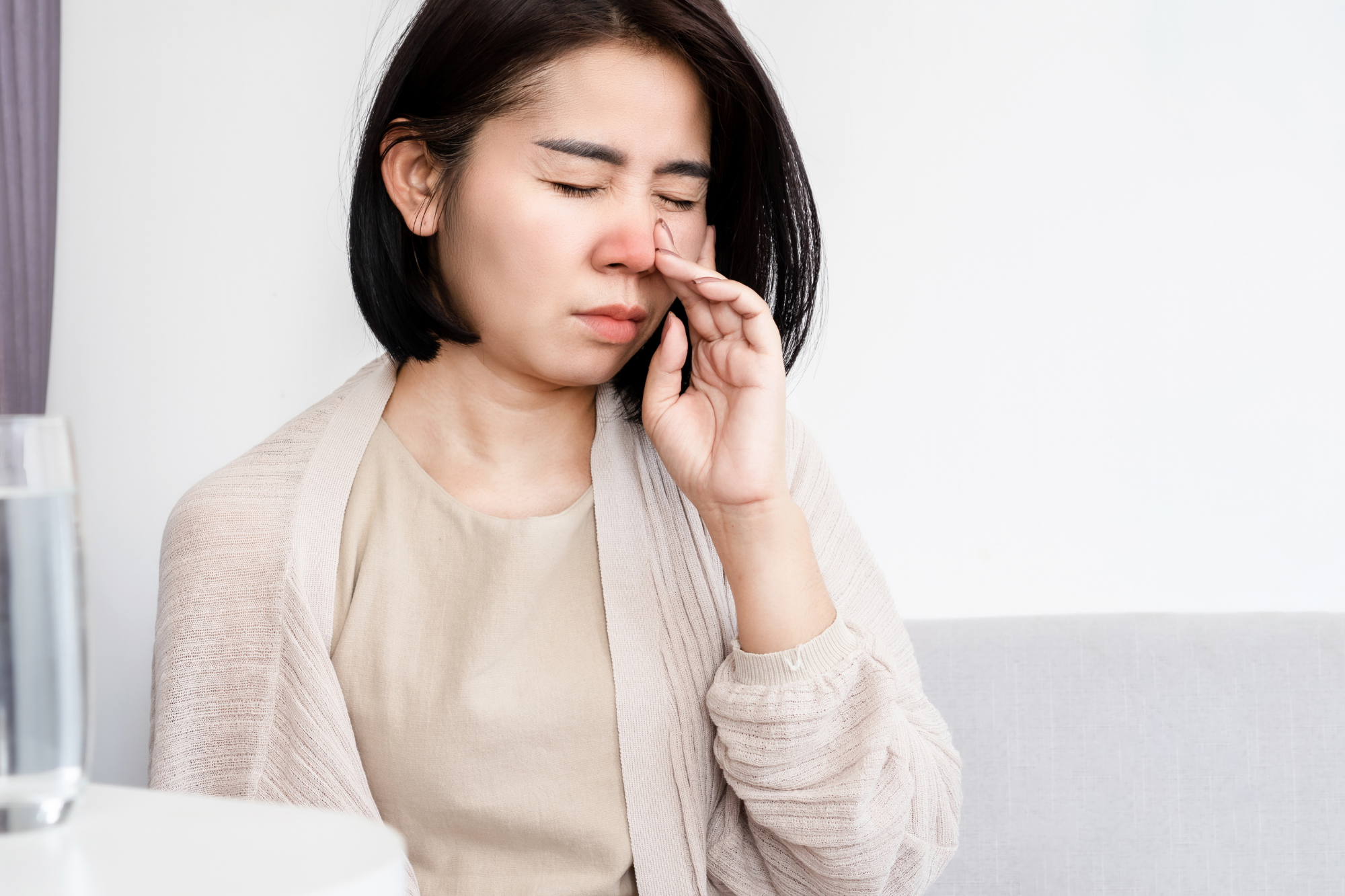 Woman holding her nose in discomfort, experiencing symptoms of a blocked nose.