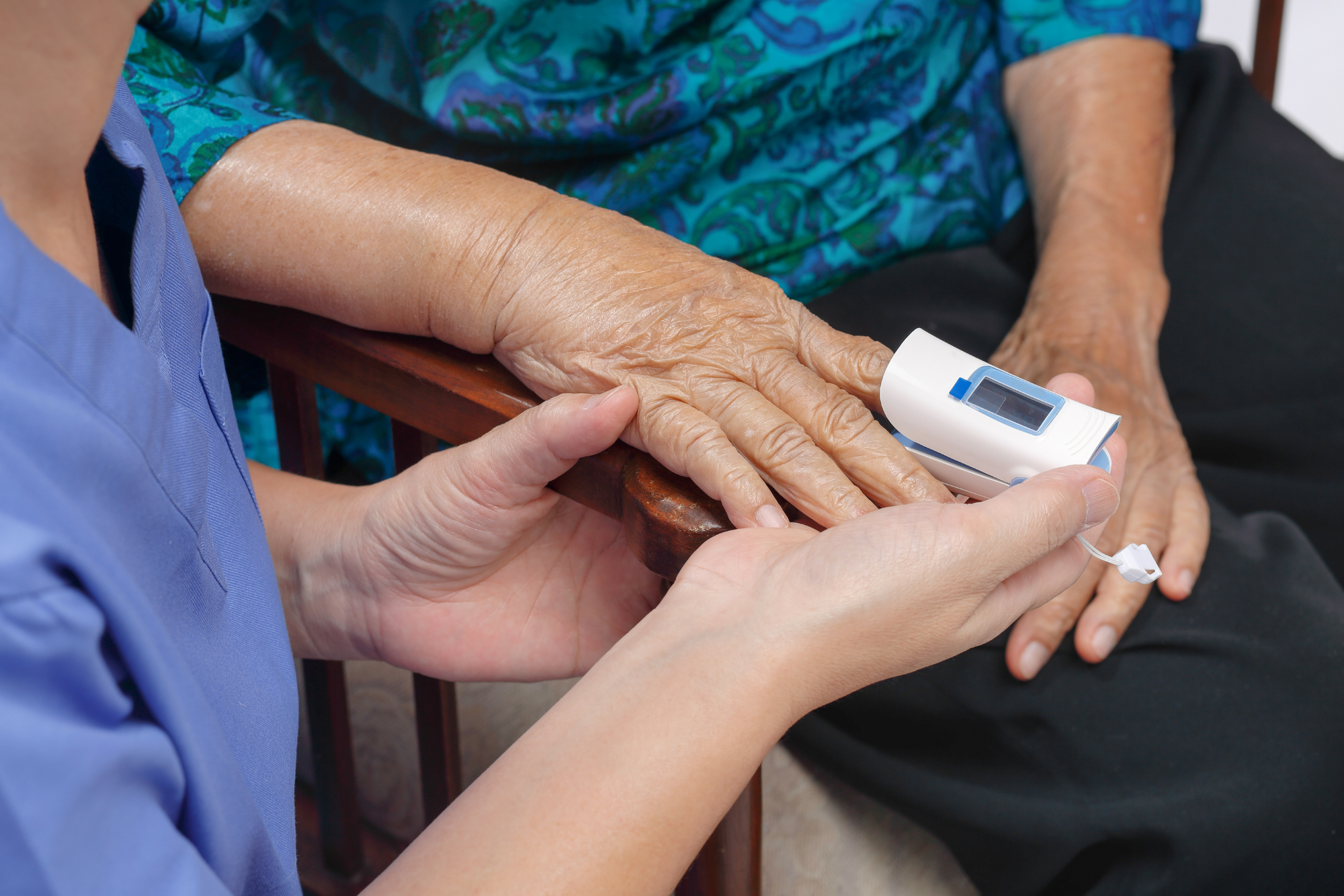 Healthcare professional using an oximeter to measure oxygen saturation on an elderly patient’s finger.