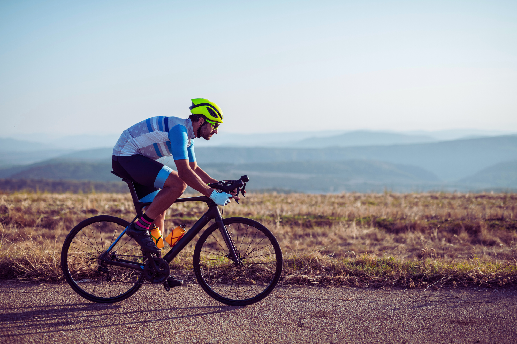 Road cyclist speeds along mountain route, wearing professional cycling gear.