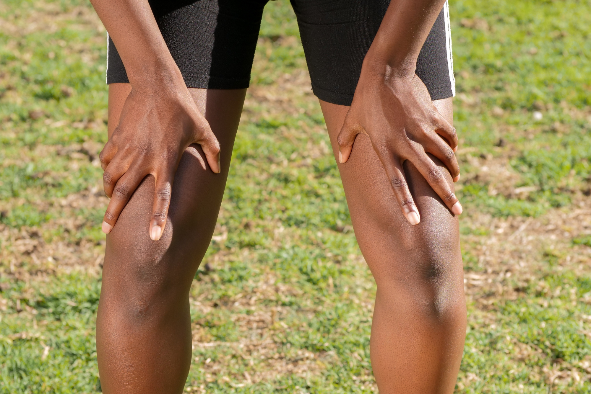 A close-up of a person resting their hands on their knees outdoors, highlighting the importance of knee health and care.