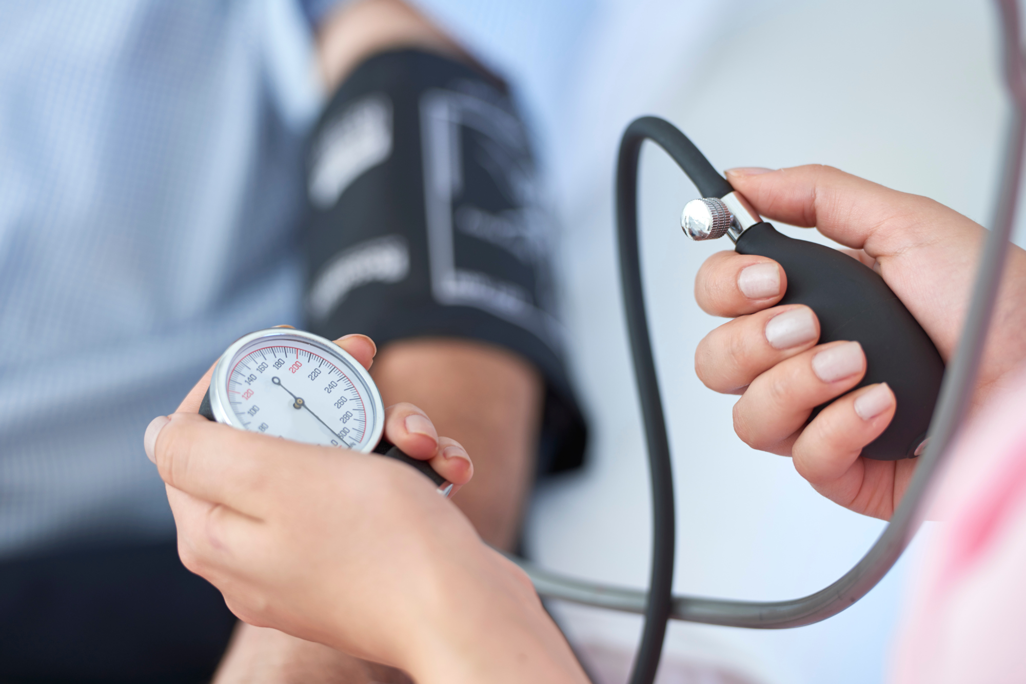 Close-up of hands holding blood pressure monitor gauge and cuff during diastolic pressure measurement.