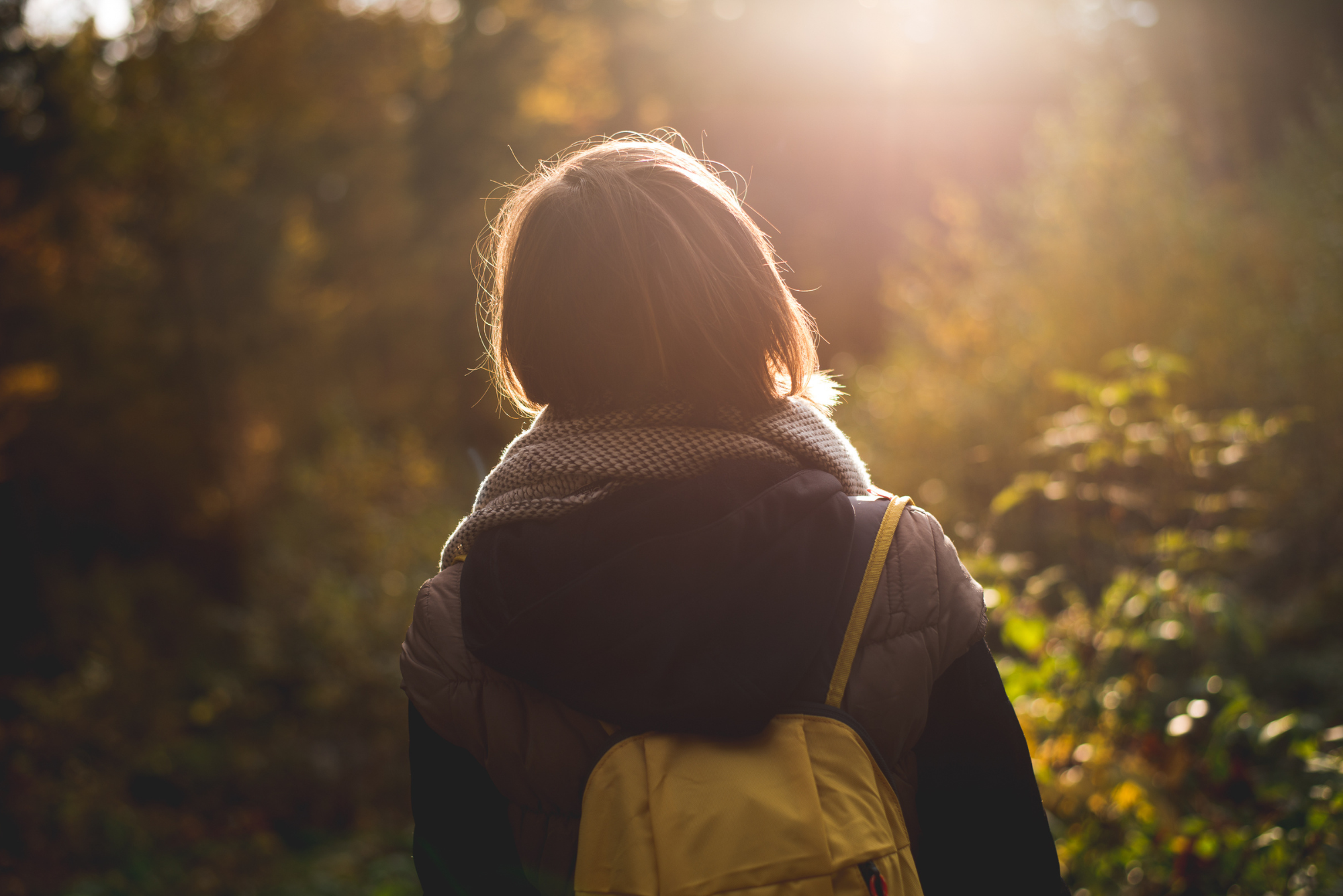 A person wearing a scarf and backpack standing in a sunlit forest, symbolizing natural ways to fight depression.