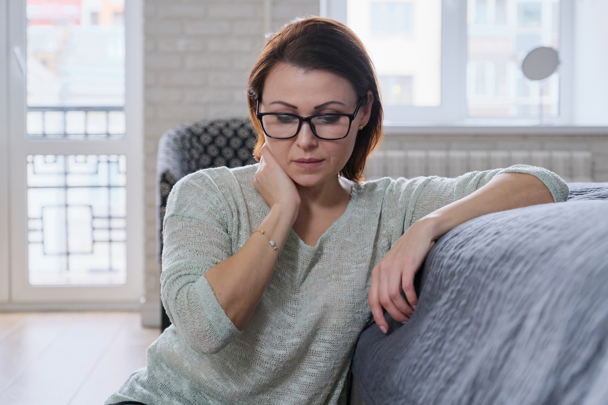 Thoughtful woman sitting in her living room, reflecting, representing concerns about perimenopause.