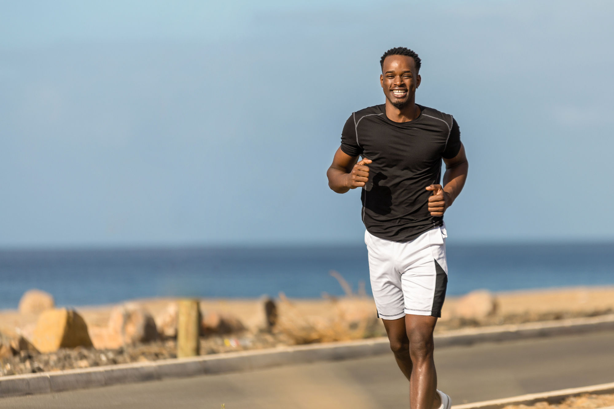 A fit man jogging outdoors by the ocean, smiling and wearing athletic clothing, promoting natural ways to boost testosterone.