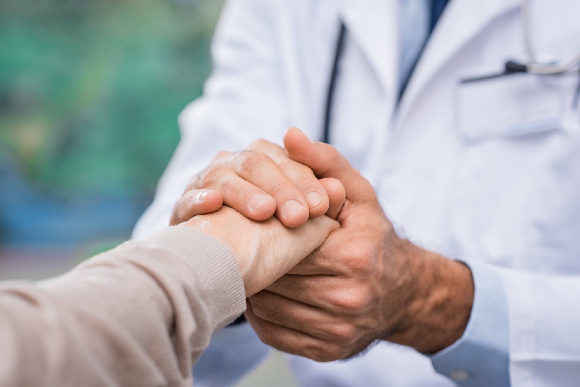 Doctor in white coat holding patient’s hands, representing supportive medical care and doctor-patient relationship.