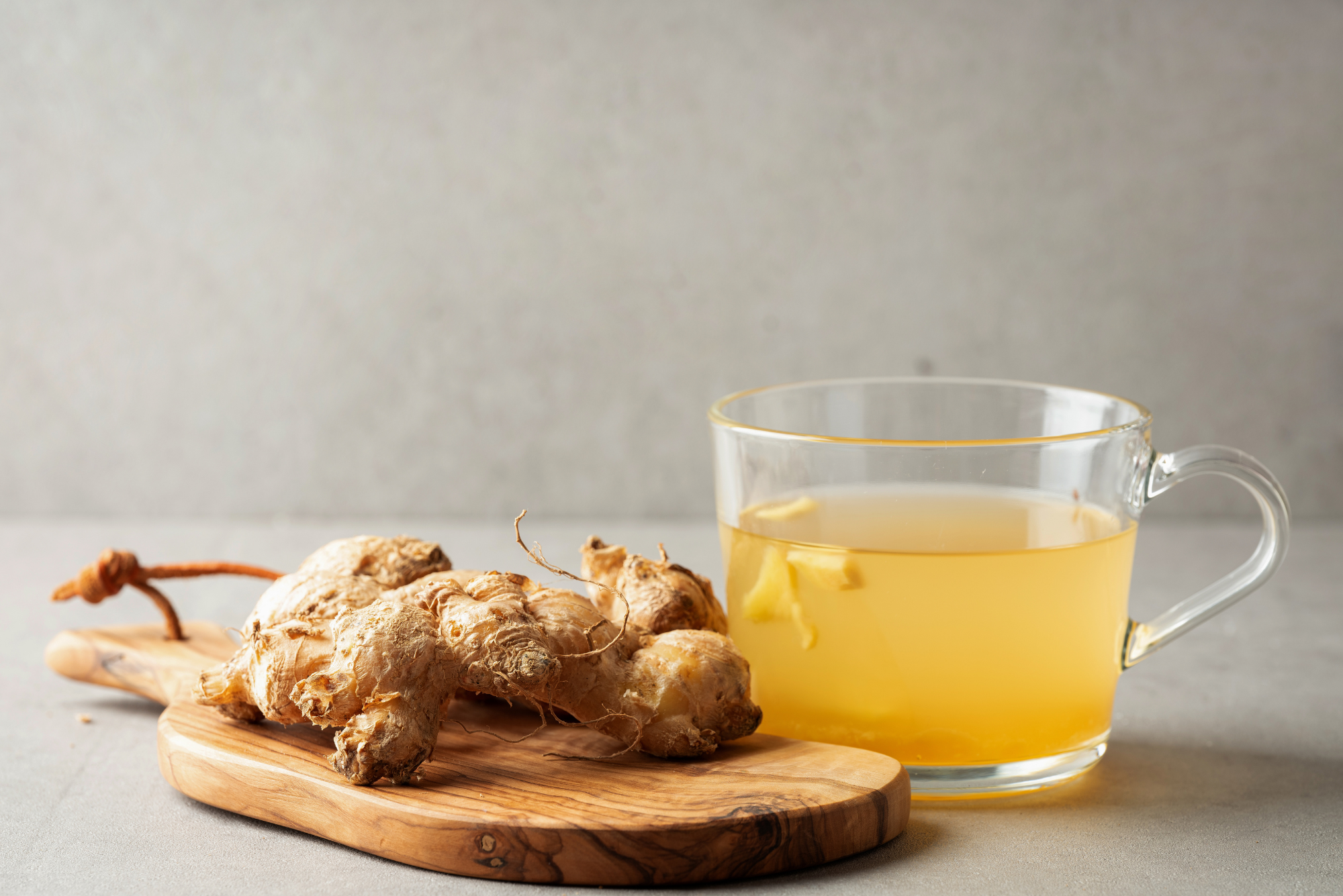 A glass cup of ginger tea with floating ginger pieces next to fresh ginger root on a wooden cutting board.