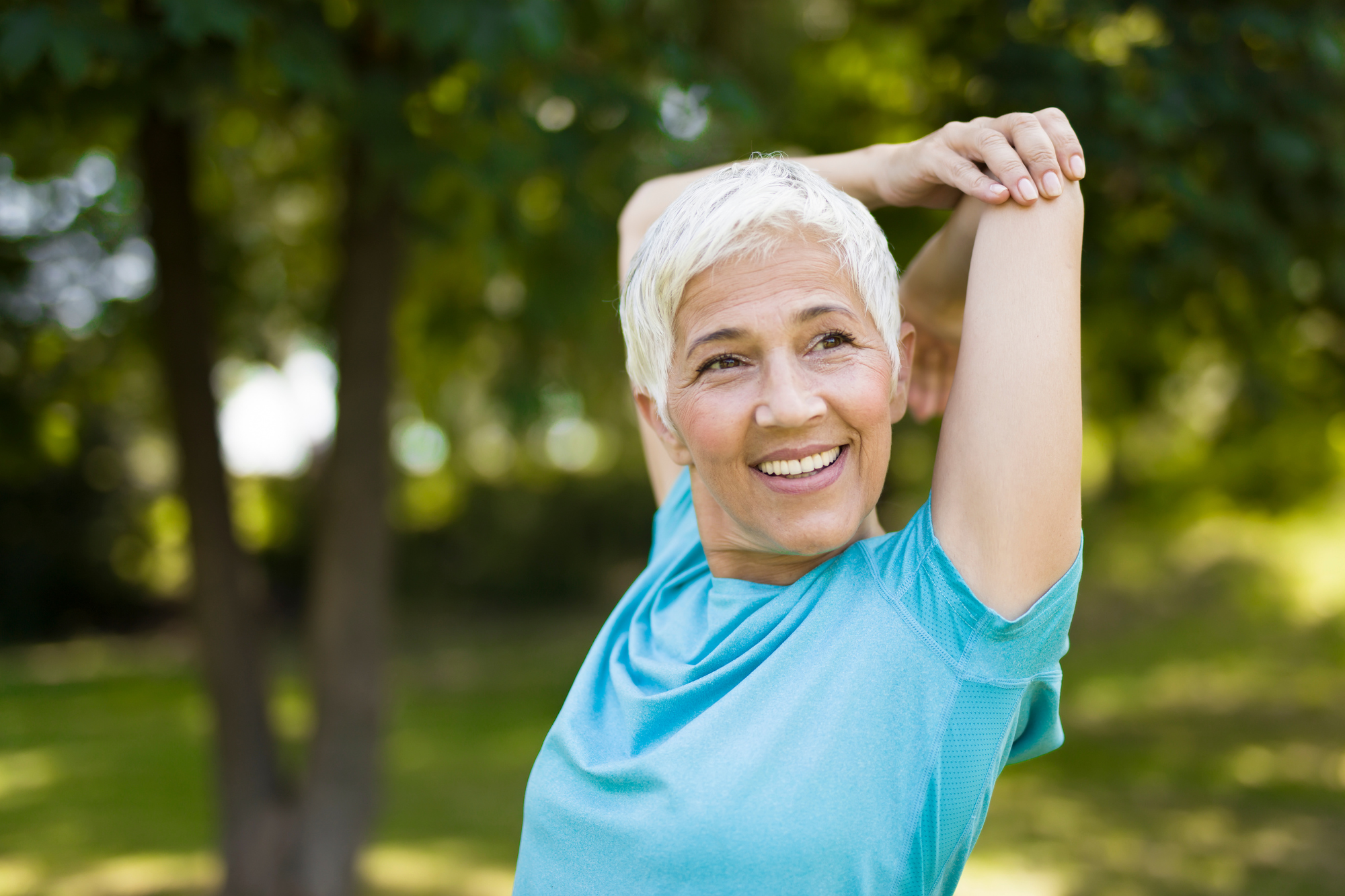 Smiling older woman stretching outdoors in a park, promoting an active lifestyle for heart health and lowering APOB levels.