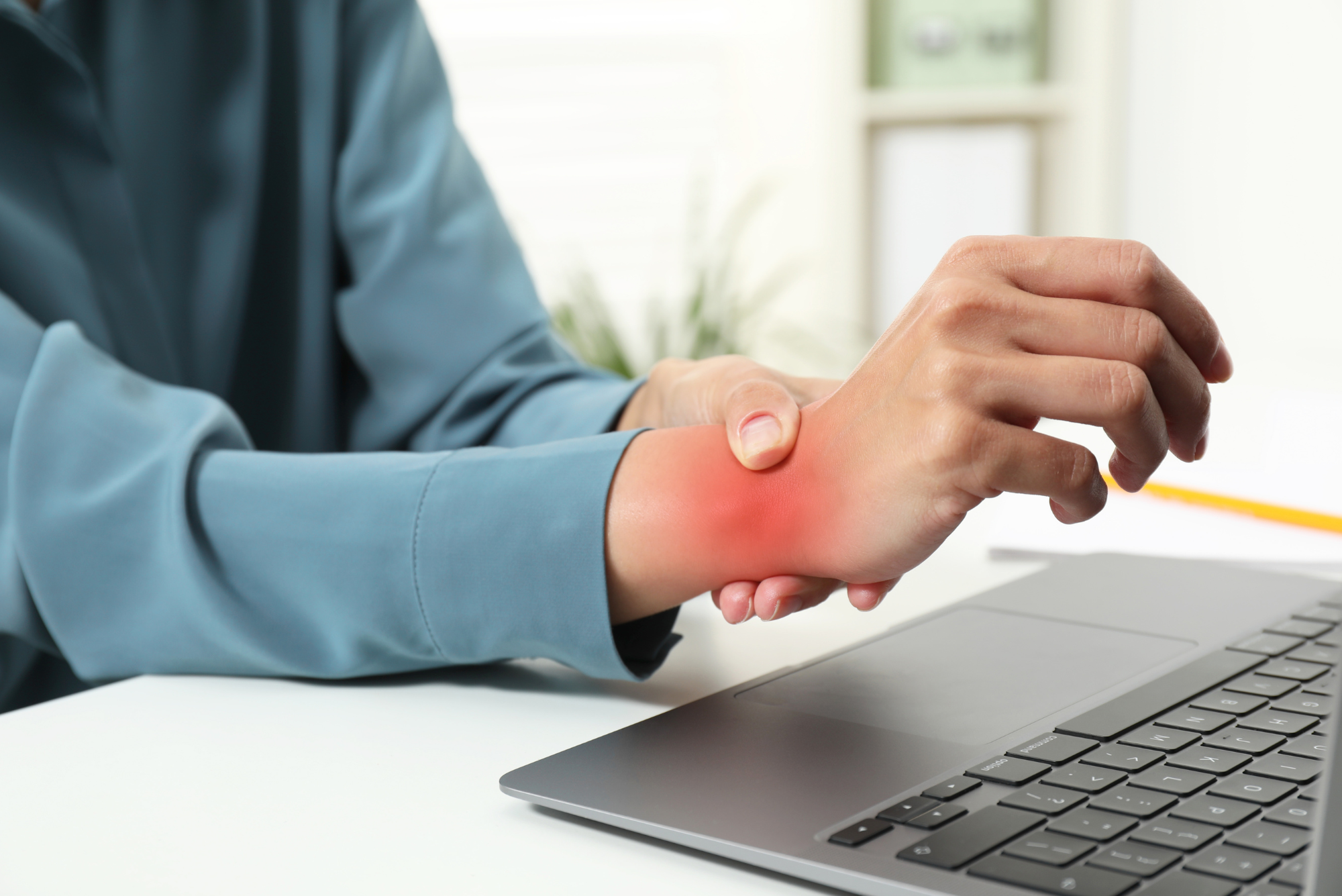 Person holding painful wrist near laptop, showing carpal tunnel syndrome symptoms.