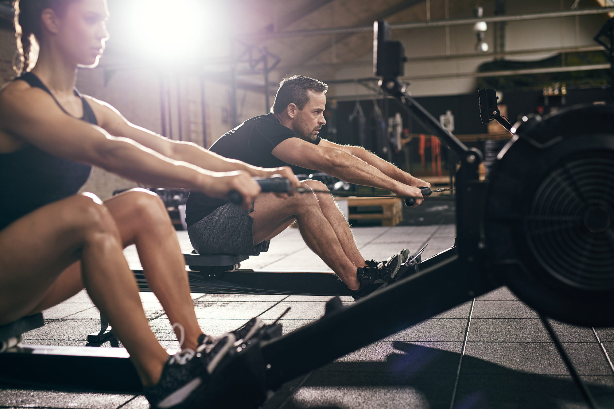 Man and woman working out on rowing machines in a gym.