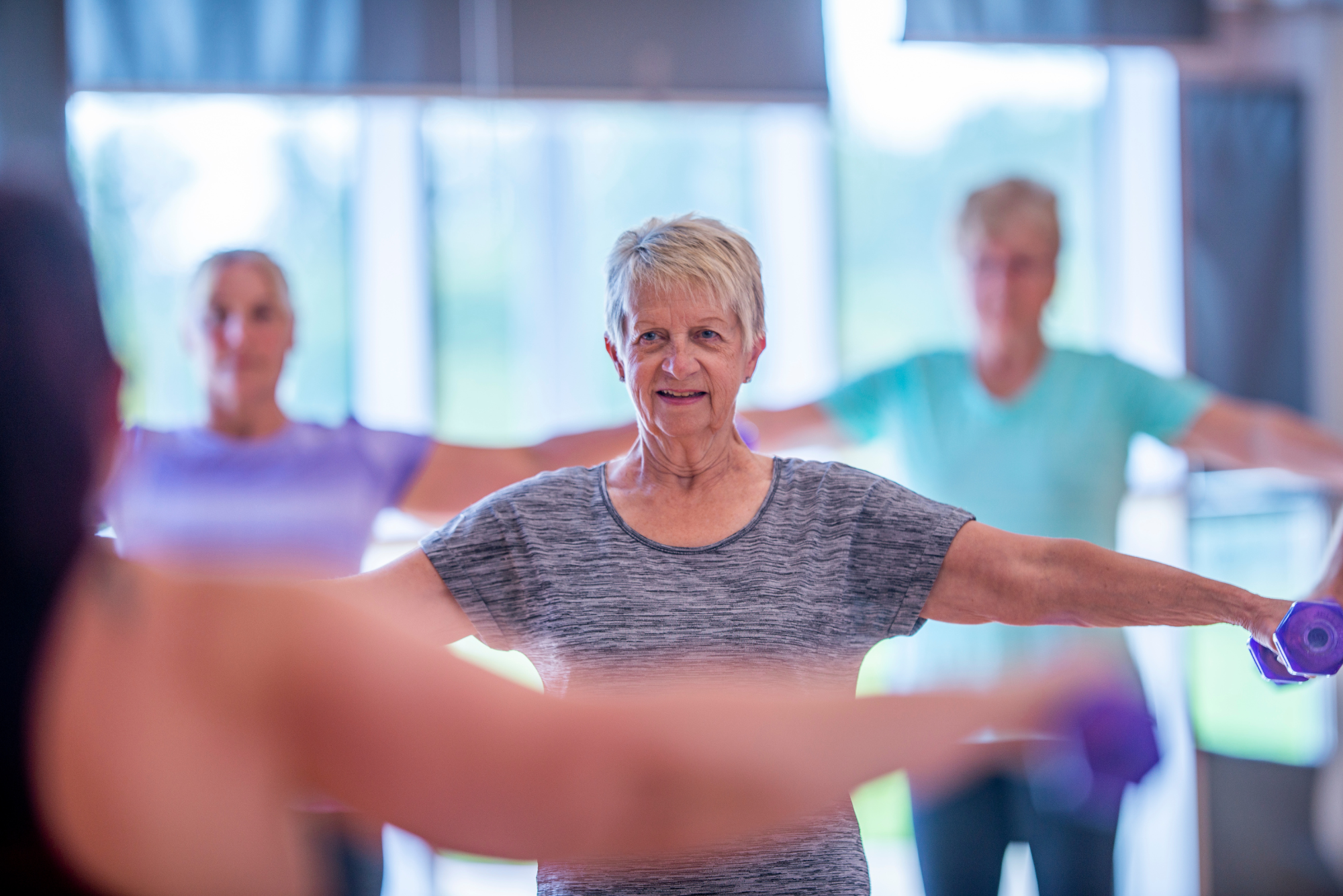 Senior woman doing resistance training with weights in gym.