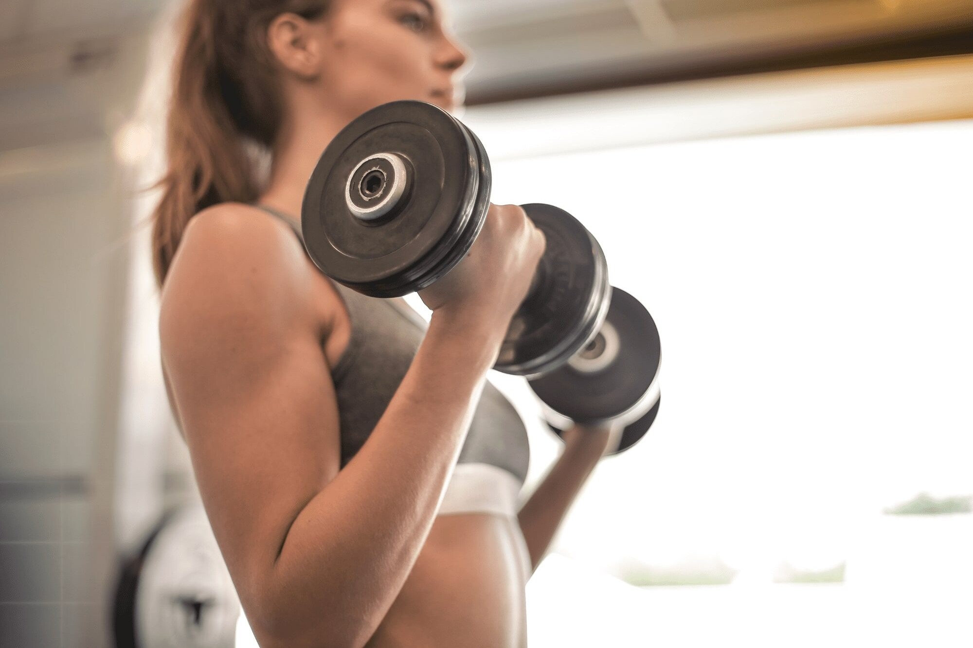 Fit young woman lifting dumbbells with focused form in gym.