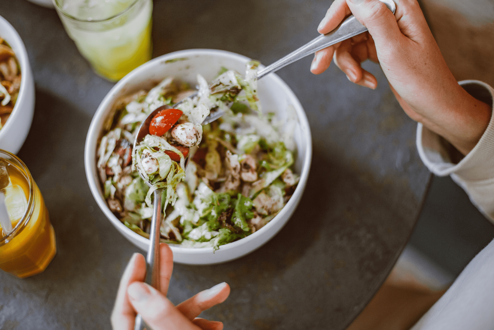Close-up of hands scooping colorful, fresh vegetable salad from bowl.