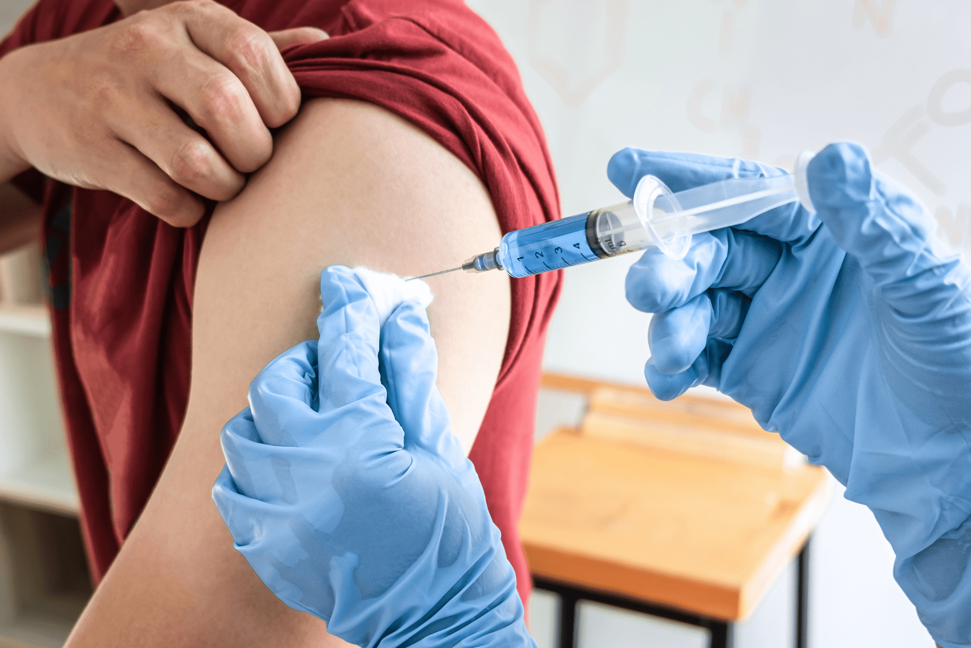 Healthcare worker in blue gloves administering vaccine injection into patient’s shoulder.