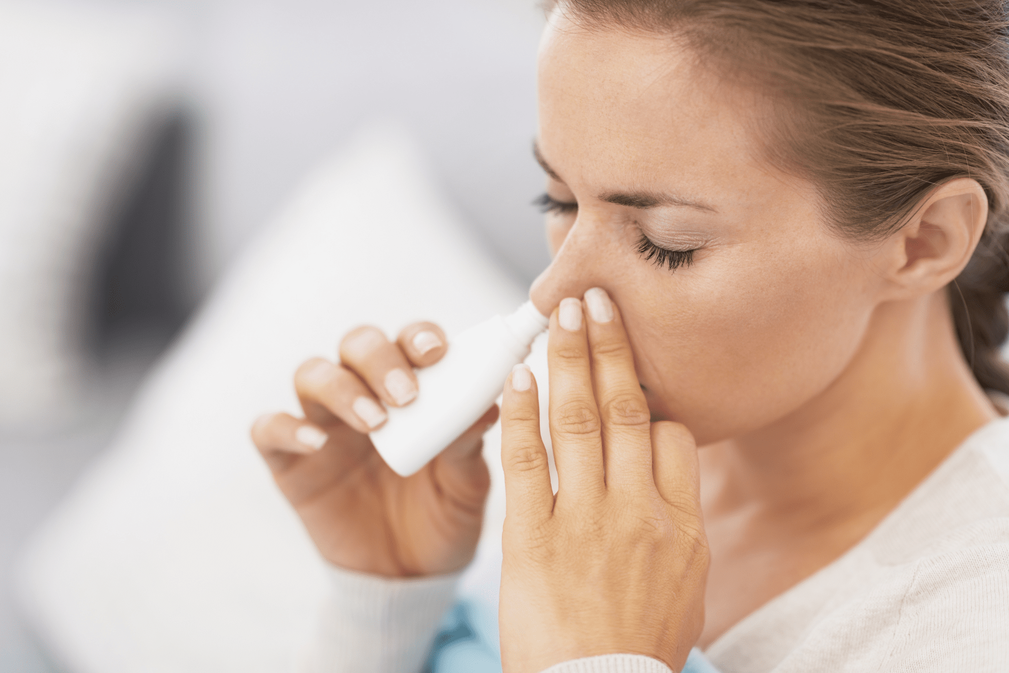 A close-up of a woman’s face as she uses a nasal spray.