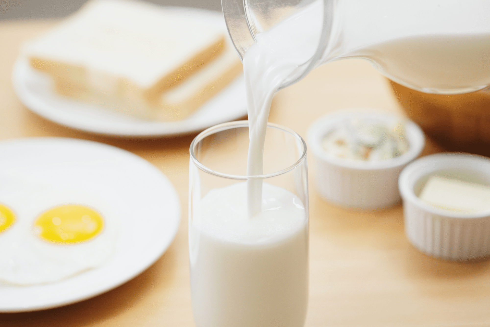Milk being poured into a glass on breakfast table.