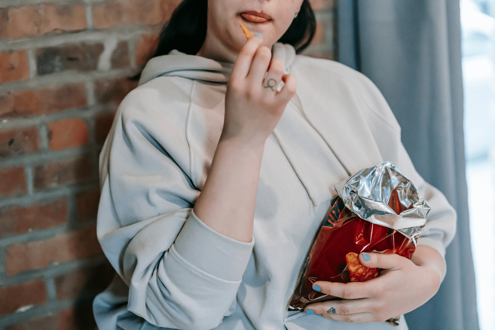 A person in a light gray hoodie eating from a bag of chips.