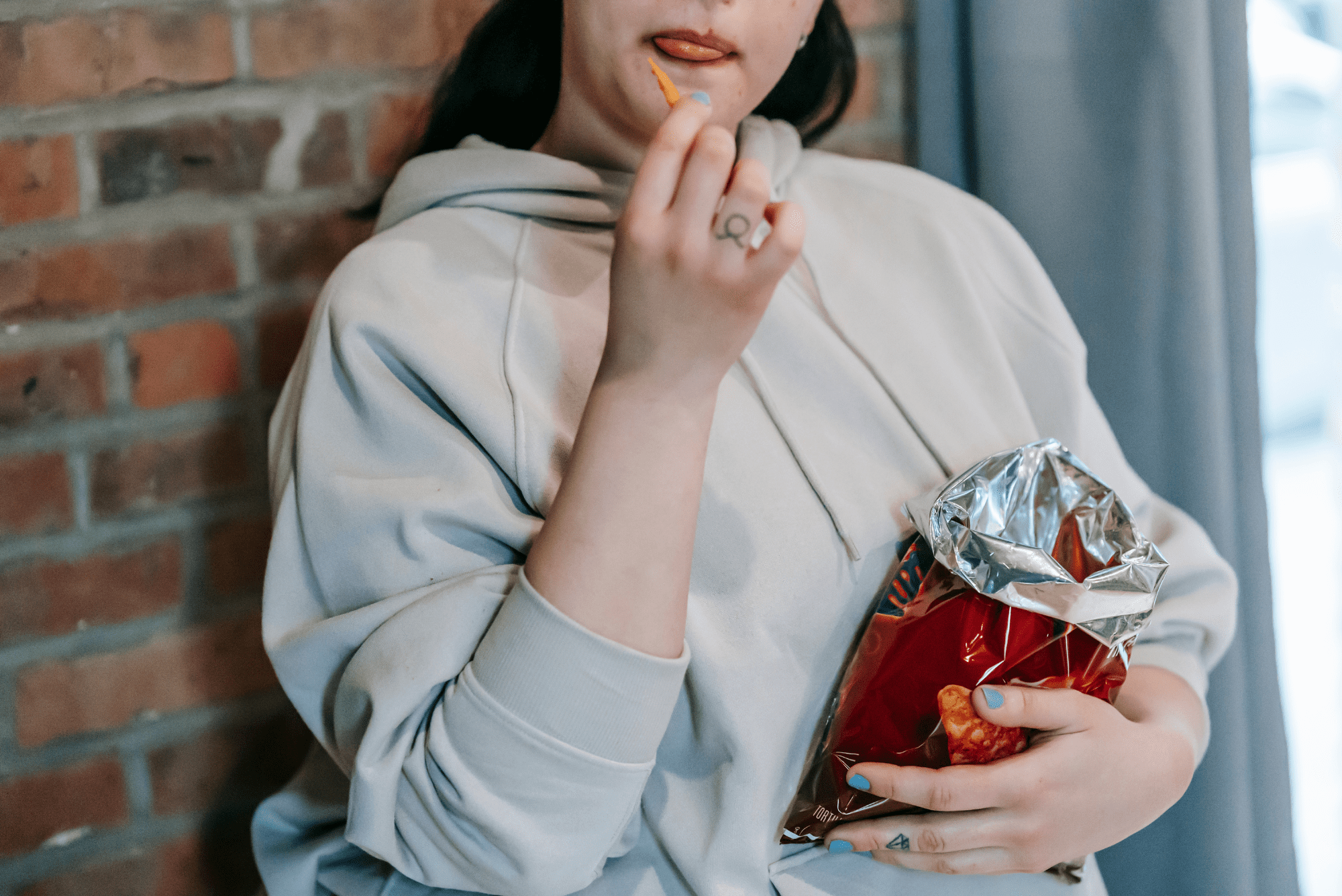 A person in a light gray hoodie eating from a bag of chips.
