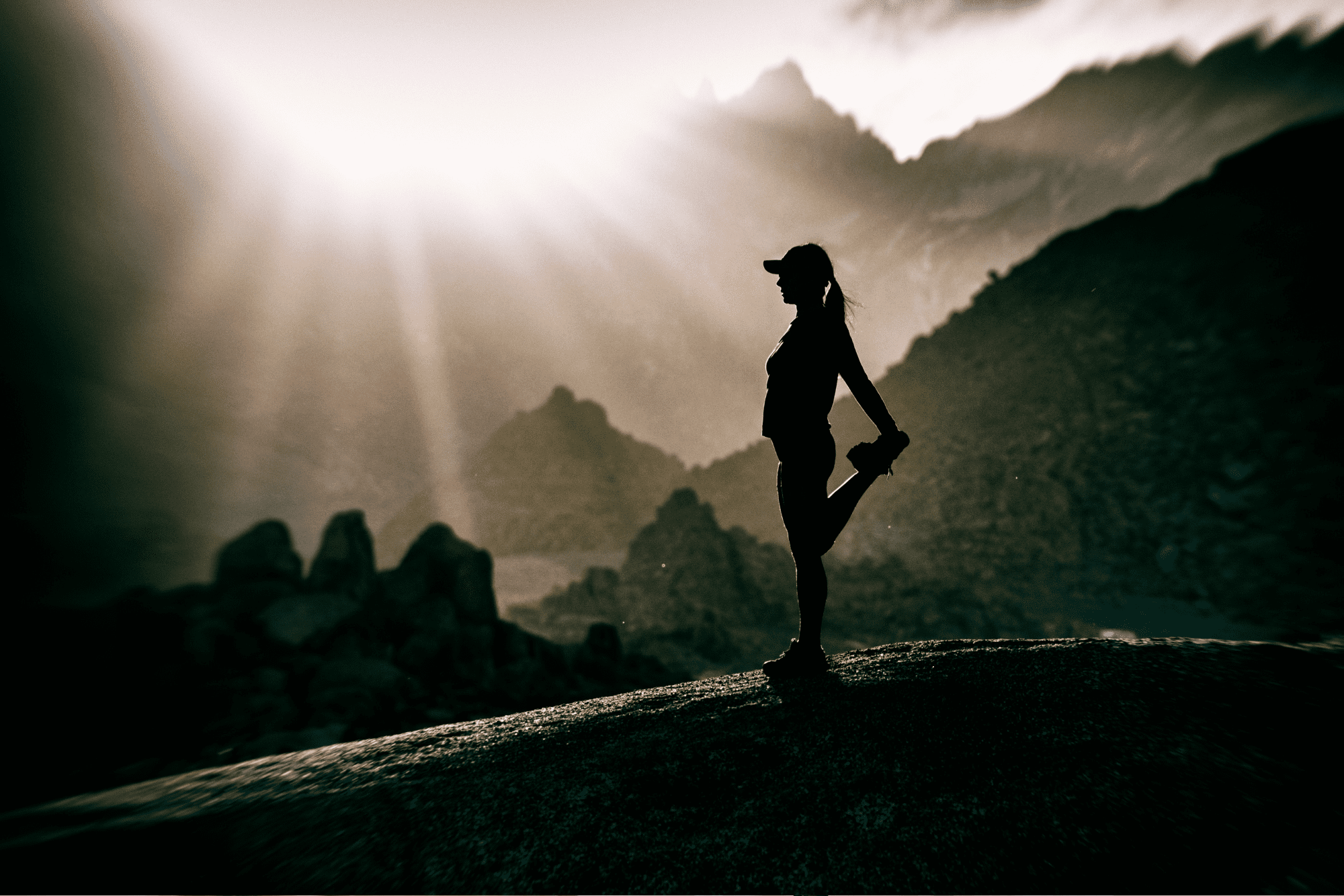 A woman on a dark mountain stretching her leg as light shines above, symbolizing resilience and metabolic reset.