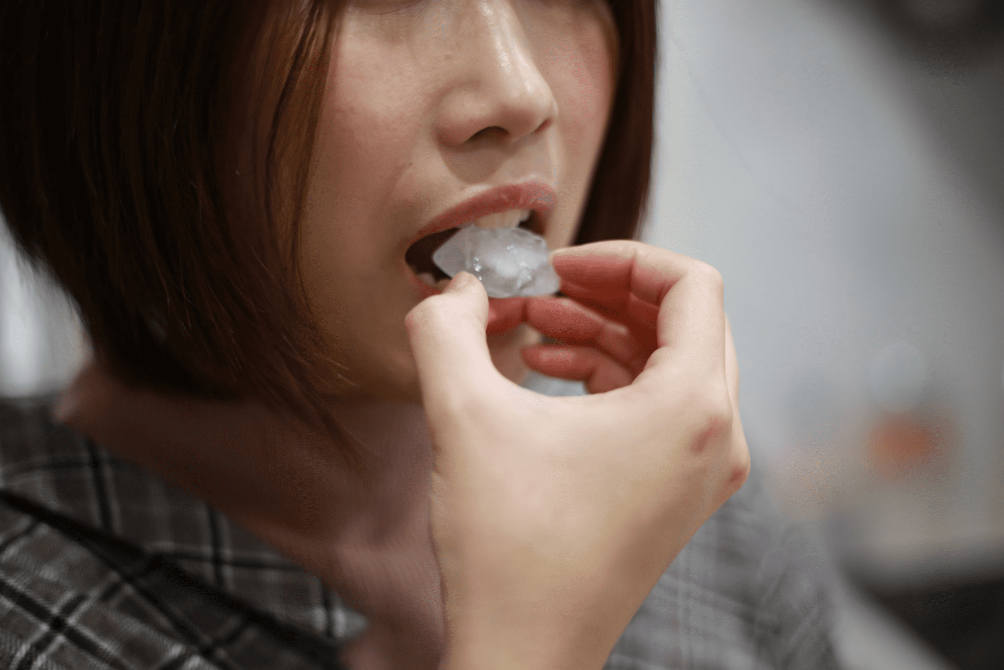 Close-up of a woman putting an ice cube in her mouth.