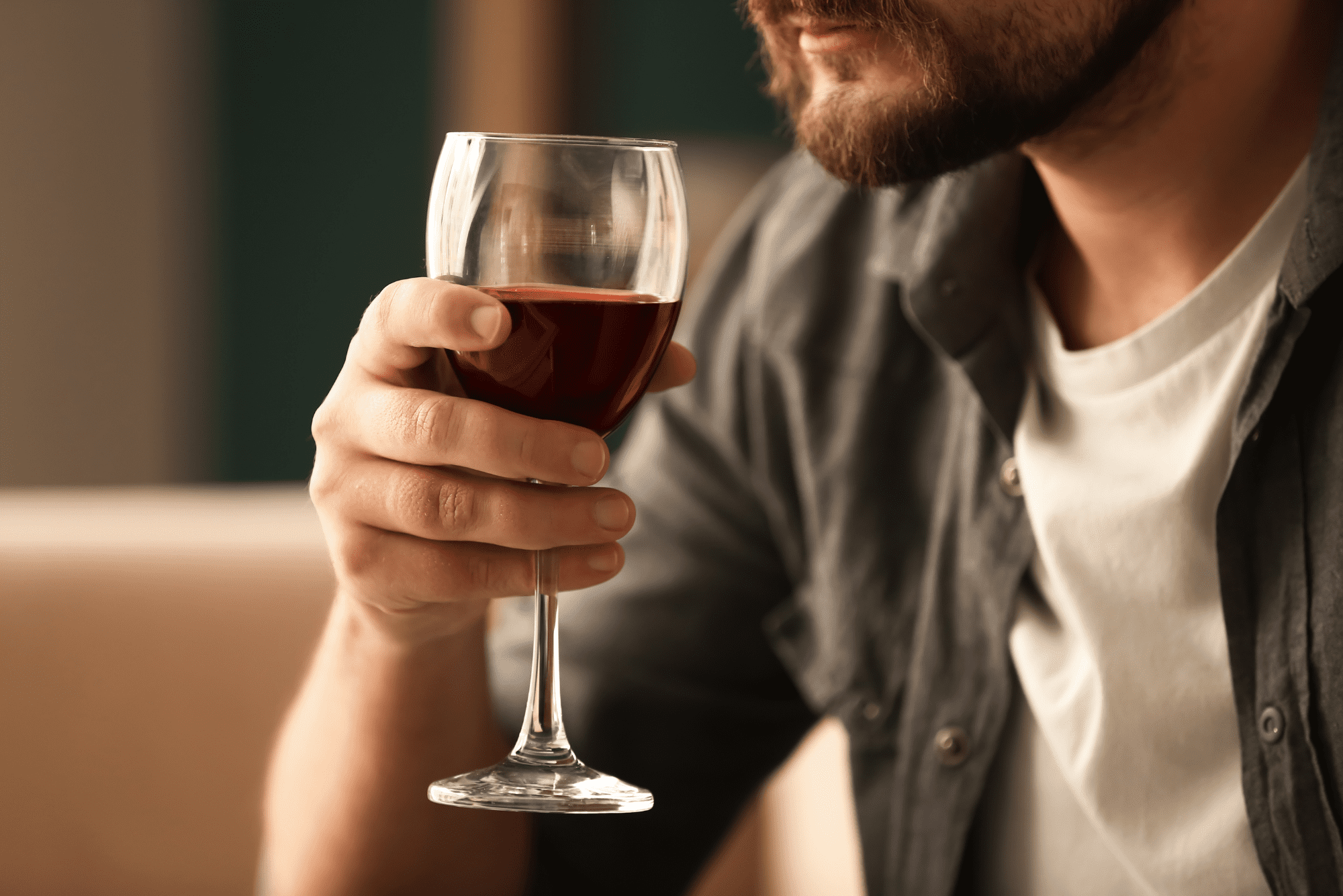Close-up of a man casually holding a glass of red wine, hinting at questions about whether alcohol causes inflammation.