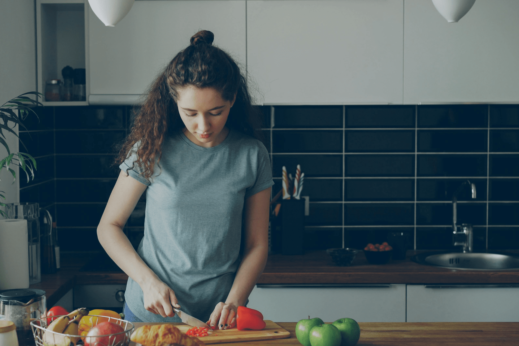 Woman chopping a red bell pepper on a cutting board.