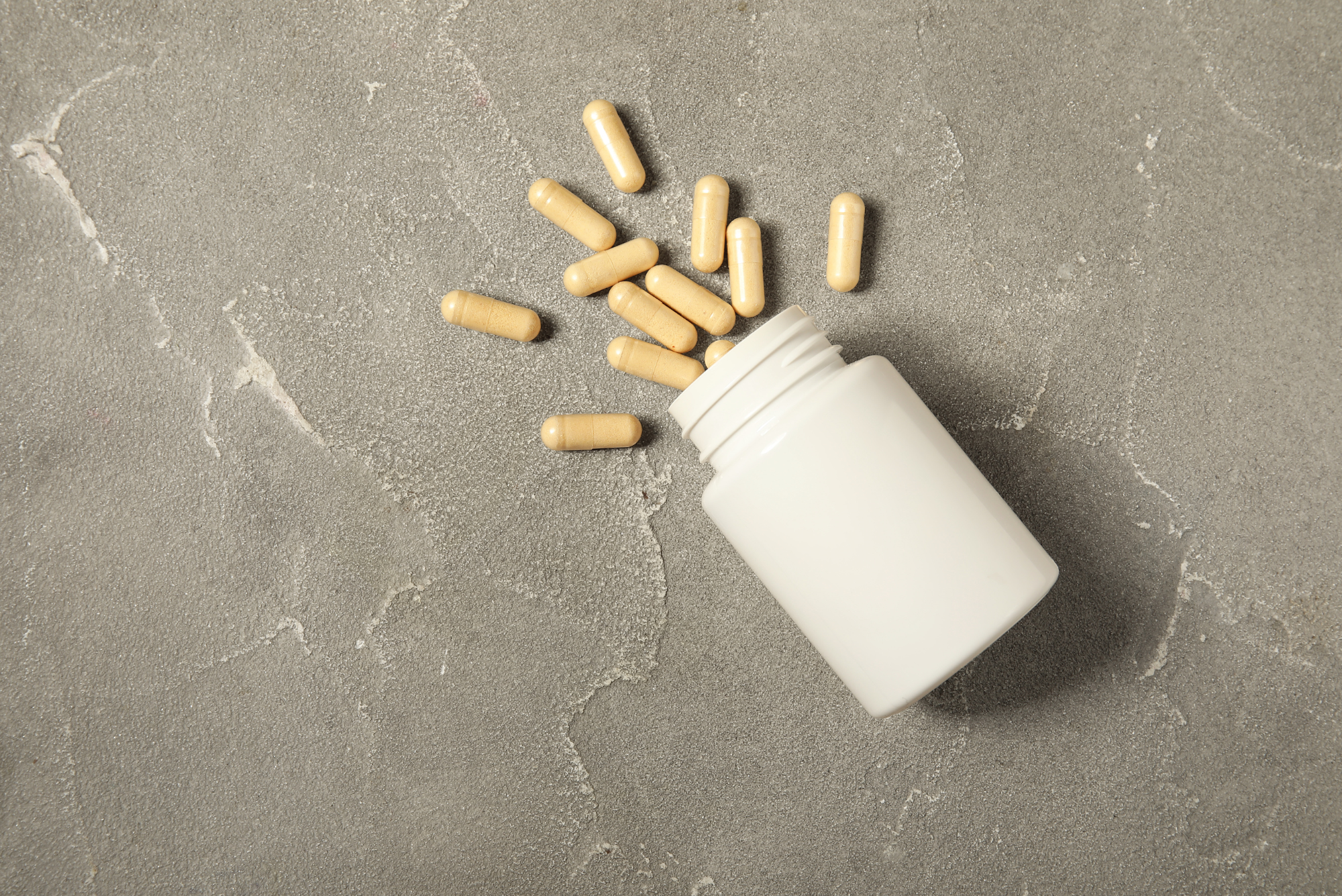 Tan supplement capsules spilled from a white bottle onto a gray stone surface, illustrating berberine benefits.