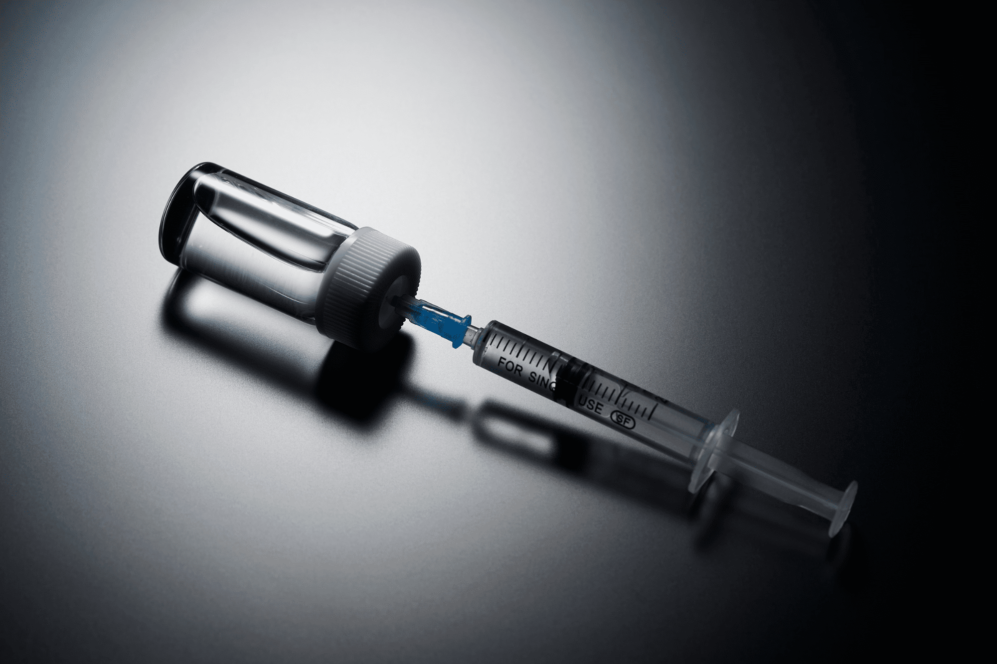 A syringe inserted into a glass medication vial.