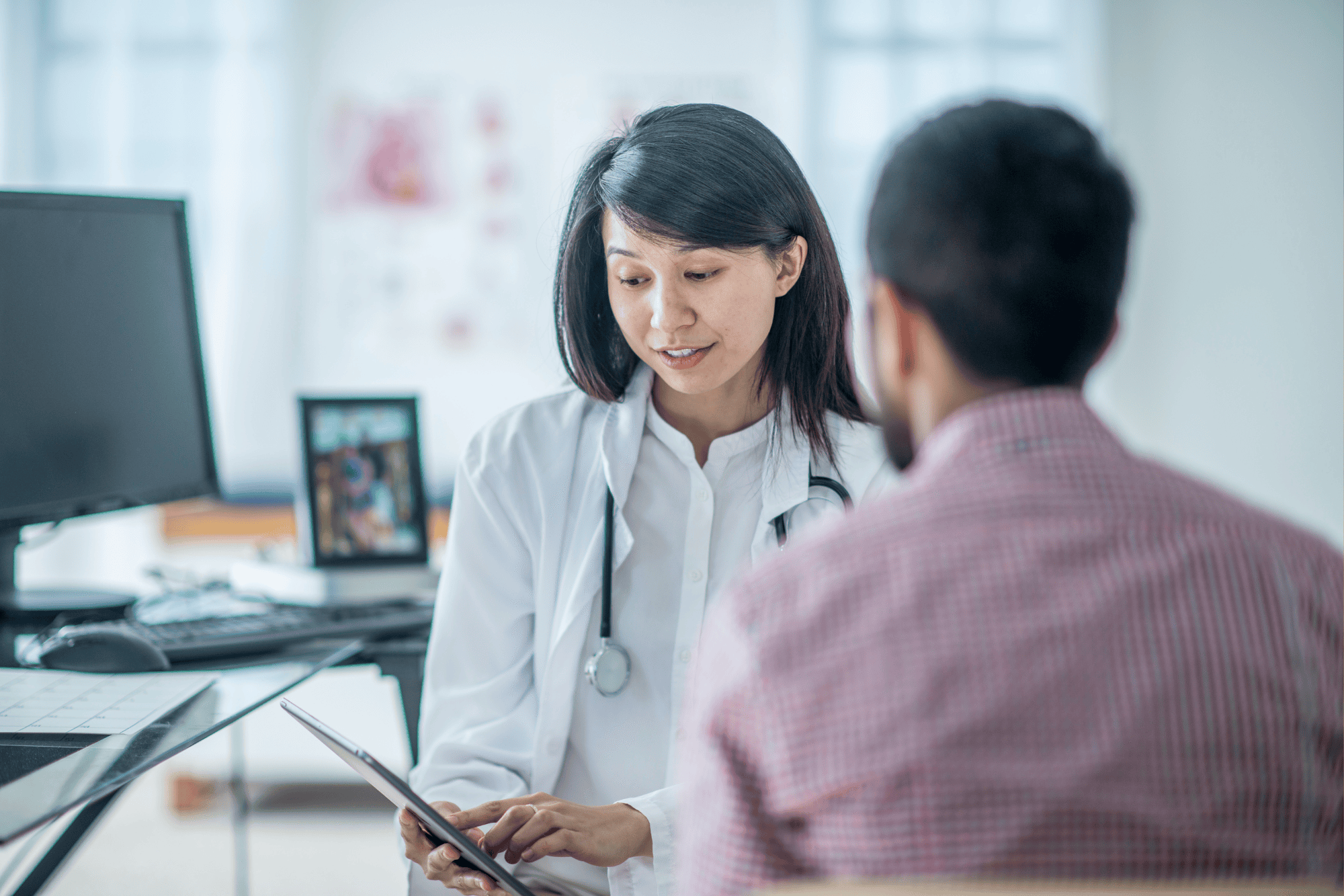 A physician reviews results from a calcium score test on a tablet with a male patient during a consultation.