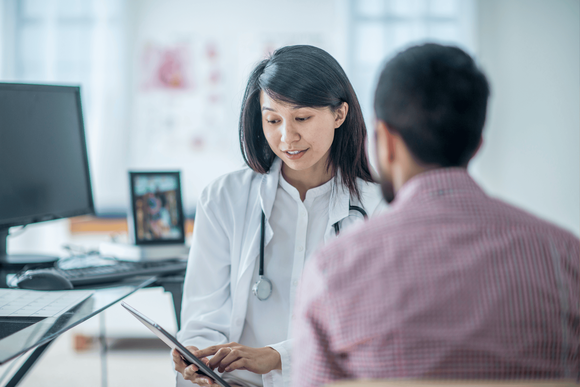 A physician reviews results from a calcium score test on a tablet with a male patient during a consultation.