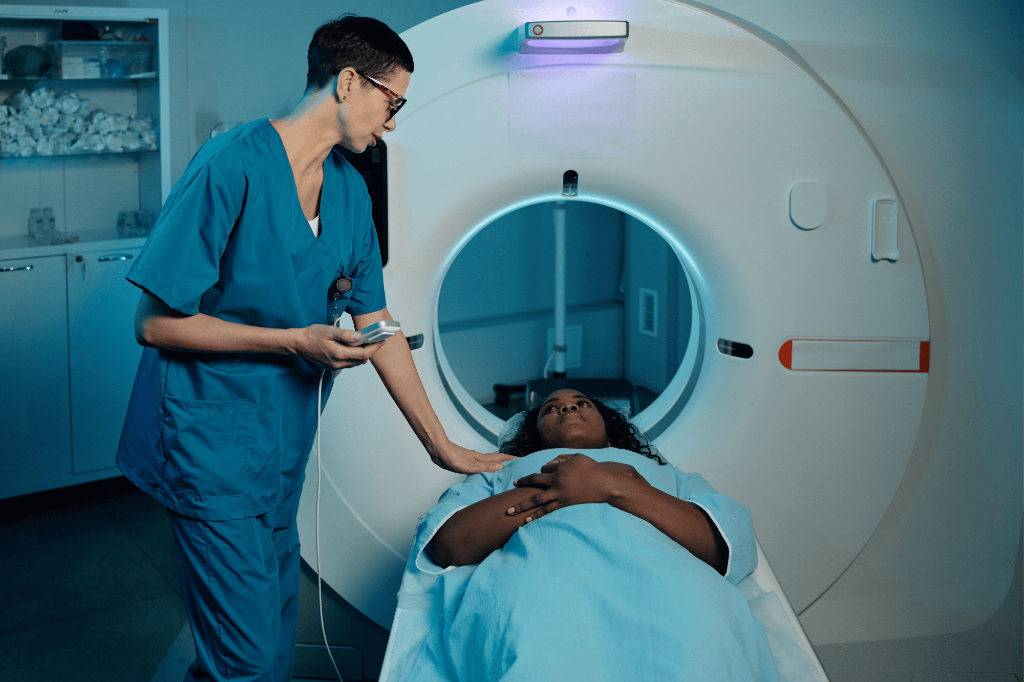 A technician comforts a patient lying on the table before entering an MRI scanner.