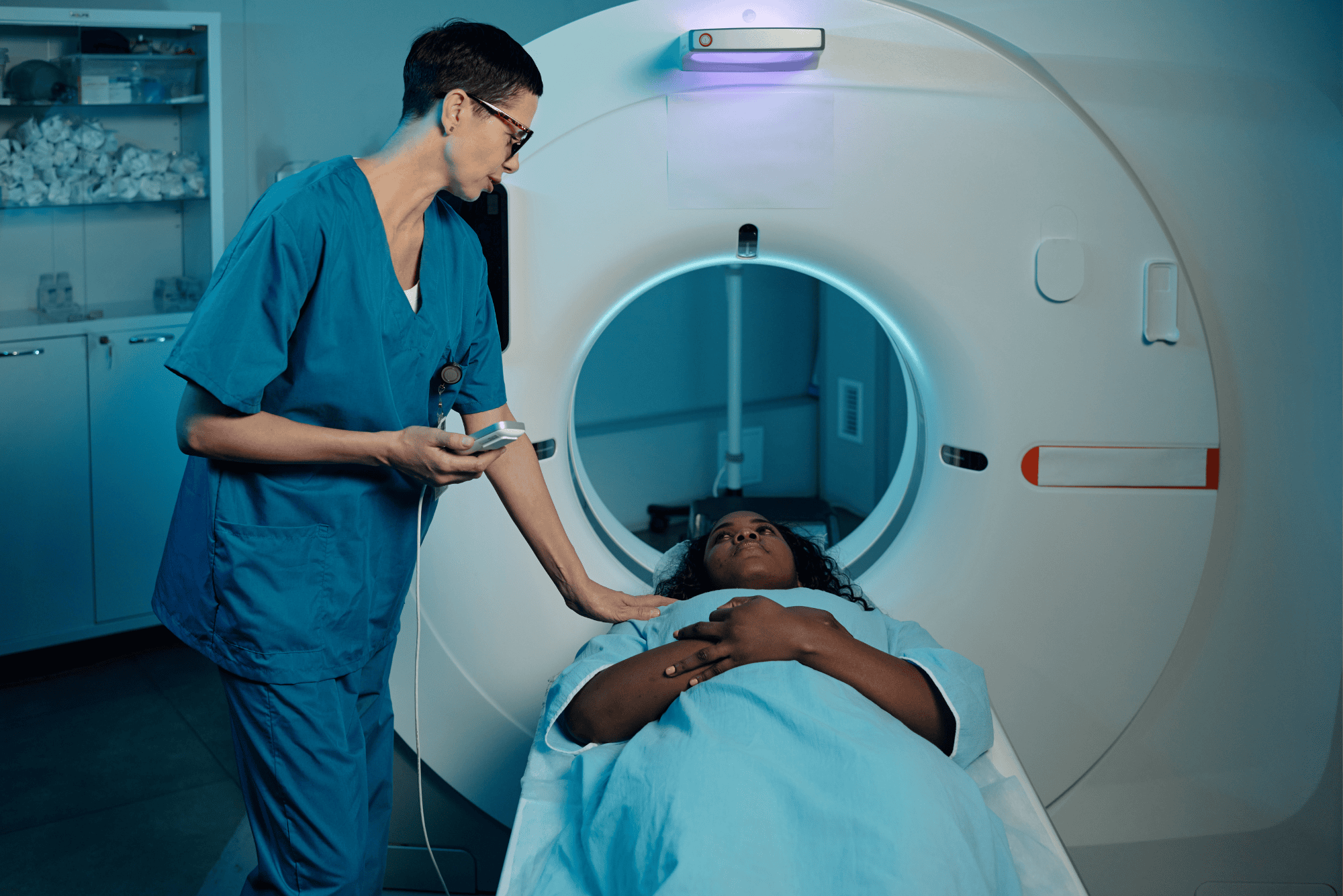 A technician comforts a patient lying on the table before entering an MRI scanner.