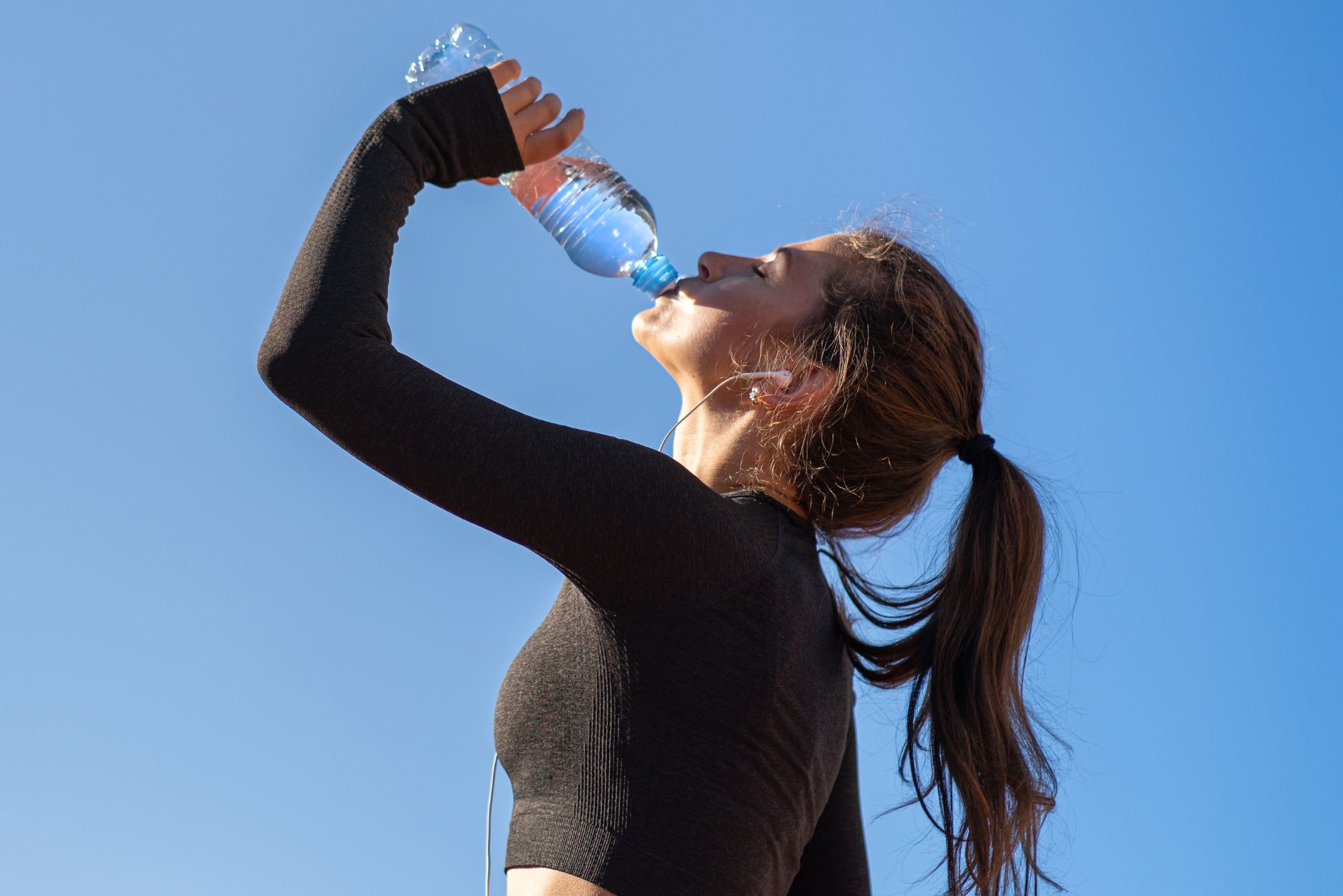 An athletic woman drinks hydrogen water out of a bottle after a long run.