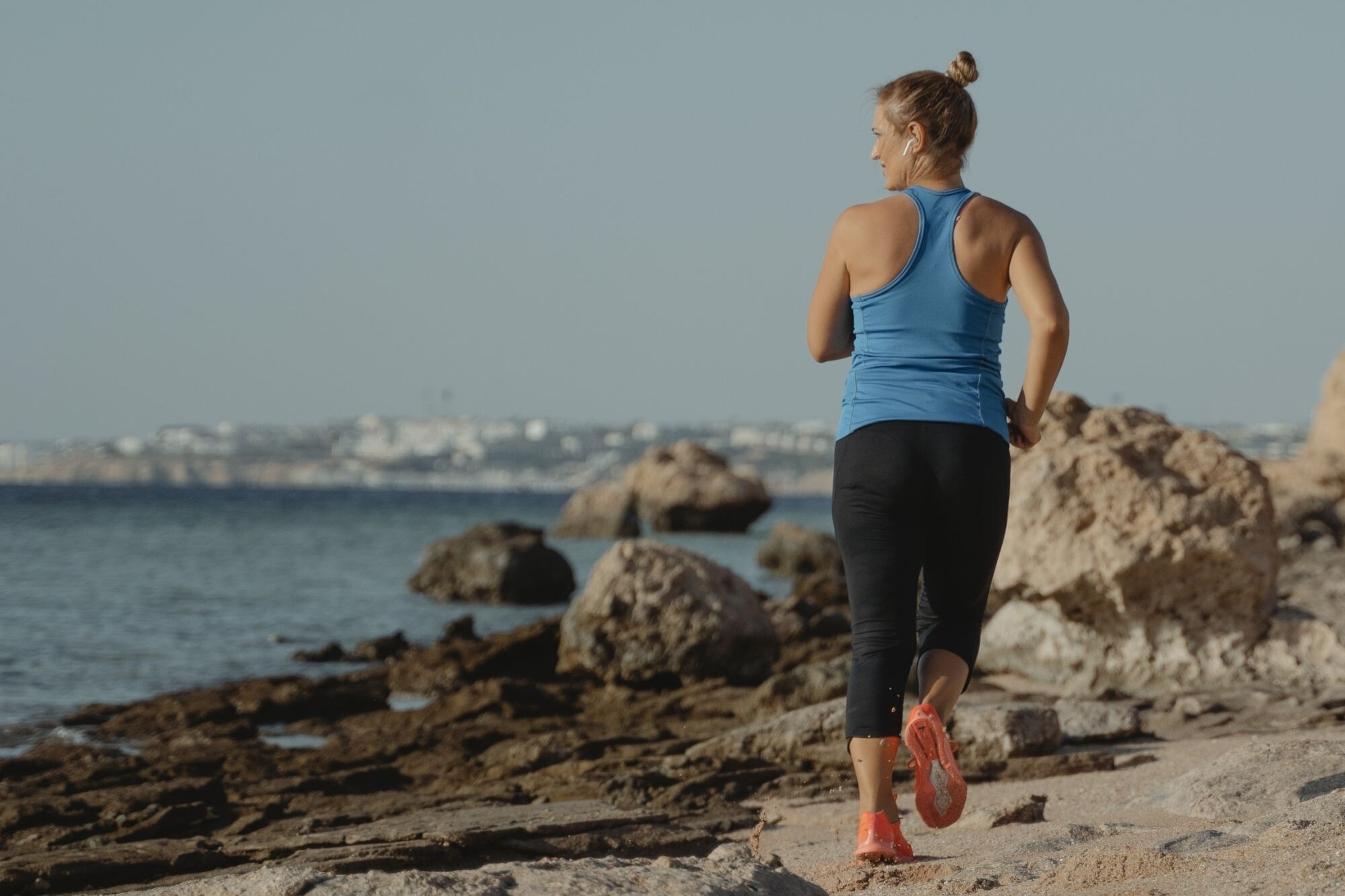 A woman jogs along the coast, smiling toward the water, living a healthy lifestyle.