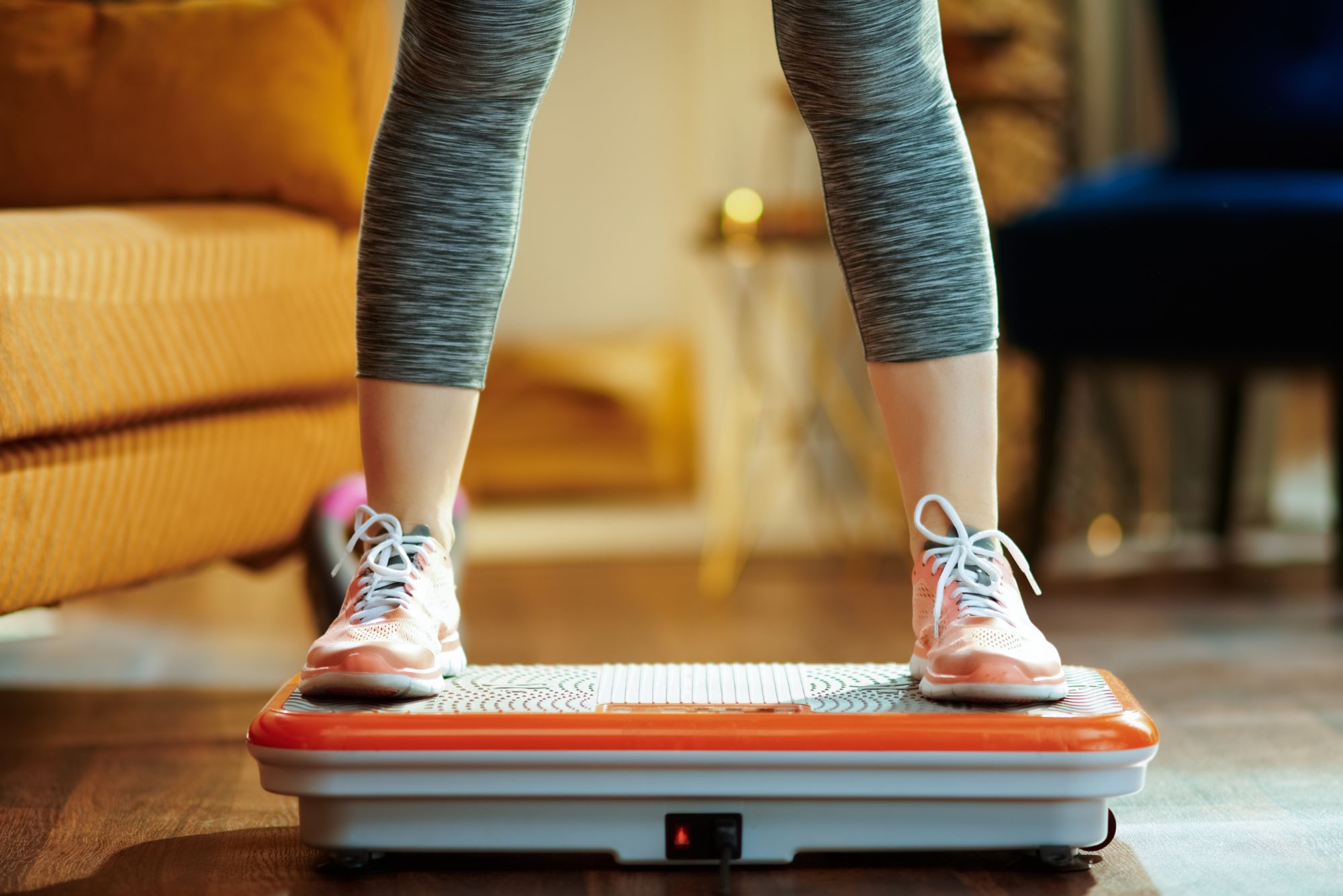 A close-up shot of woman in workout attire with feet planted firmly on a vibration plate.